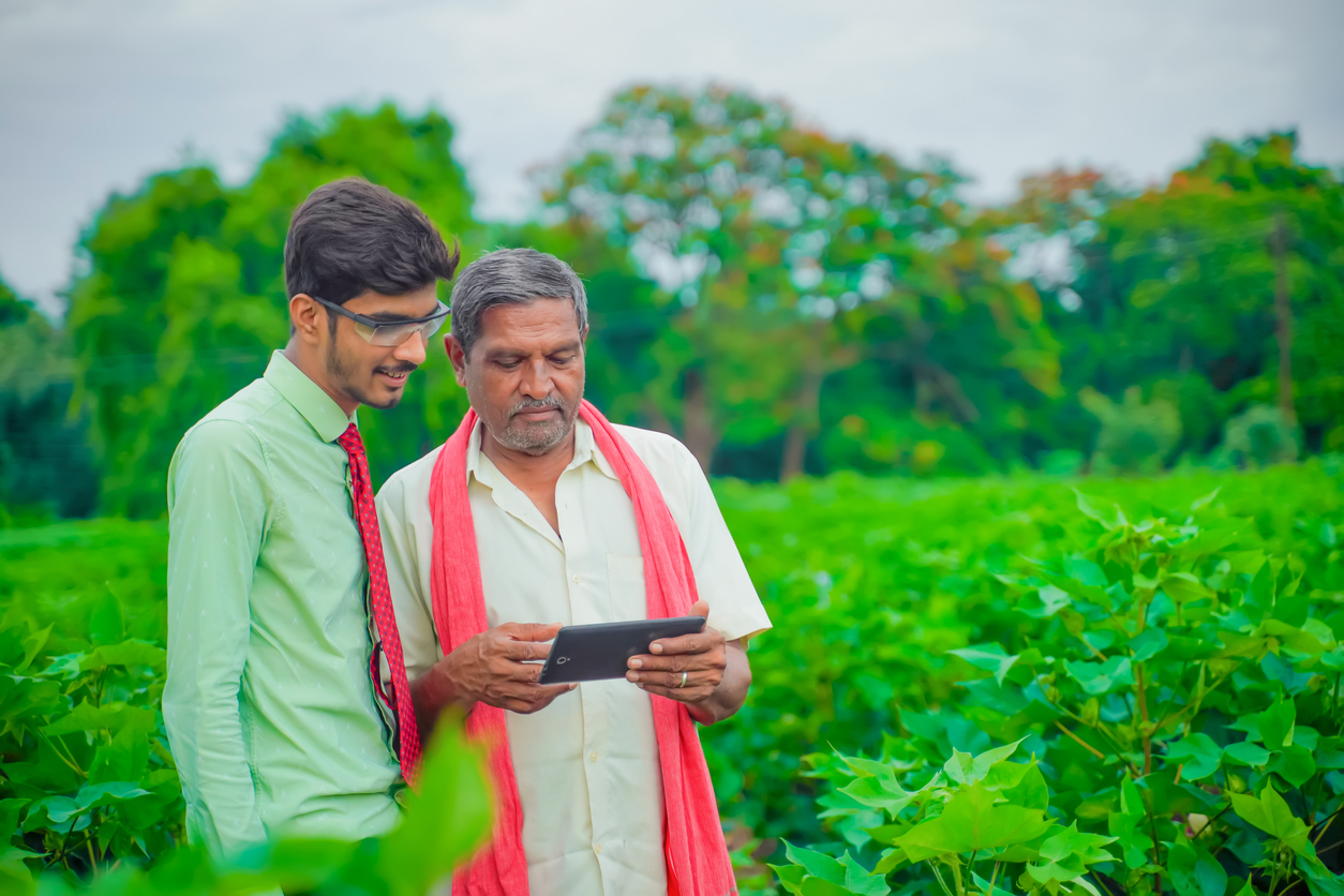 Young indian agronomist Discussing with farmer and showing some information in tablet